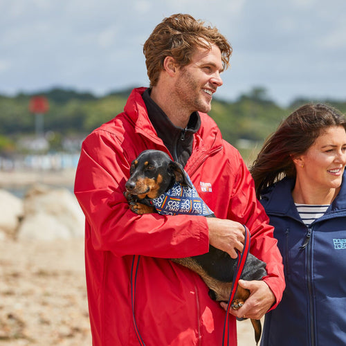 A man wearing a red jacket holding a dog in his arms.