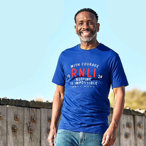 A man smiling and wearing a blue RNLI t-shirt with the text 'WITH COURAGE NOTHING IS IMPOSSIBLE' and the RNLI logo