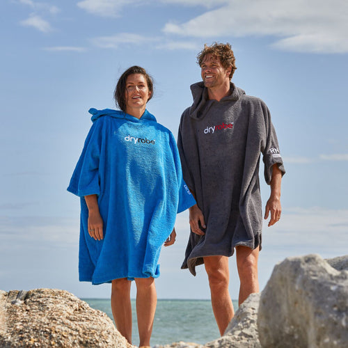 A man and a woman on a beach wearing RNLI dryrobe® Organic Towel Robes.
