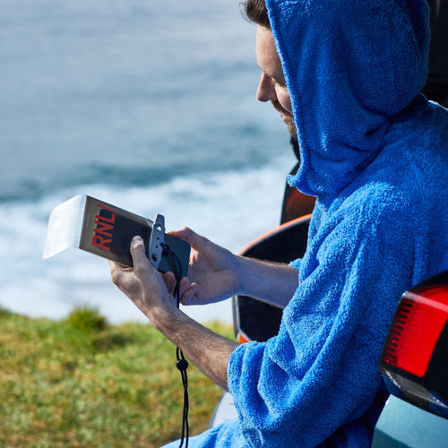 A man wearing a blue changing robe holding a waterproof phone case in his hand