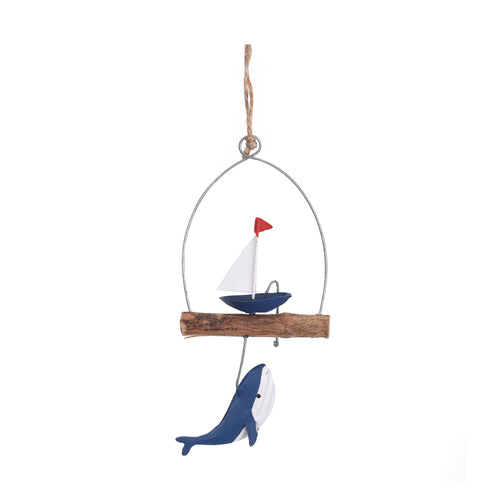A wooden hanging decoration with a sailing boat  on top of a small wooden branch. Beneath the branch hangs a wooden whale painted in blue and white