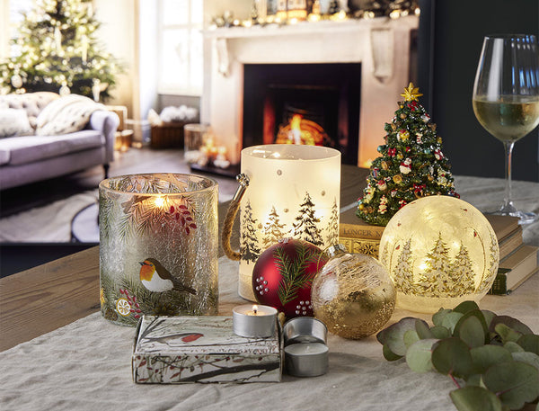 A selection of festive RNLI Christmas decorations, candles and lights on a table with a fireplace and Christmas tree in the background.