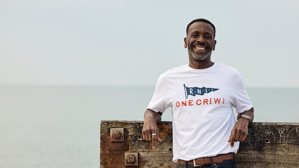  Model wearing a white t-shirt with 'ONE CREW' design, standing on a wooden platform against a light blue sky. 