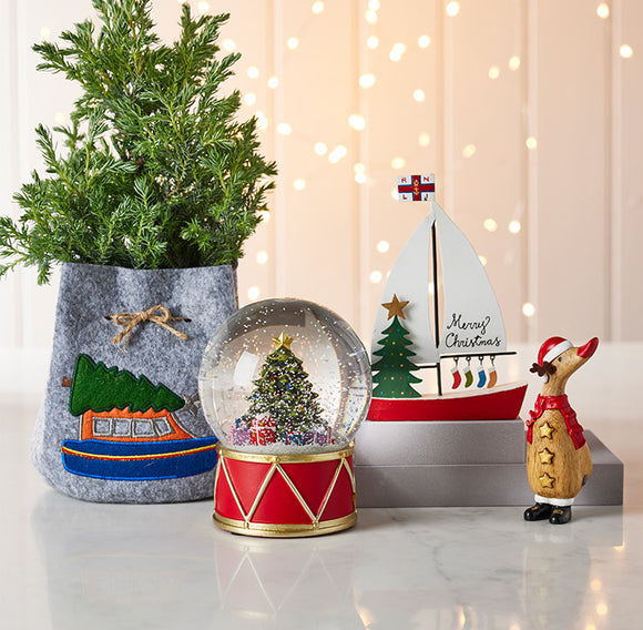  Decorative items including a potted plant, snow globe, sailboat, and Christmas tree figurine on a light background. 
