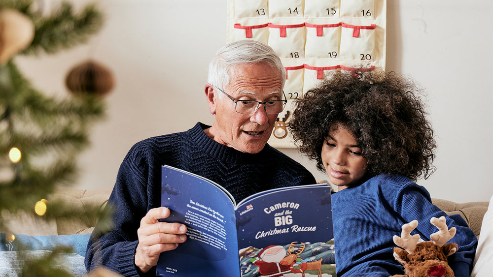  Man reading a personalised book to a child in a festive setting with a Christmas tree and calendar. 