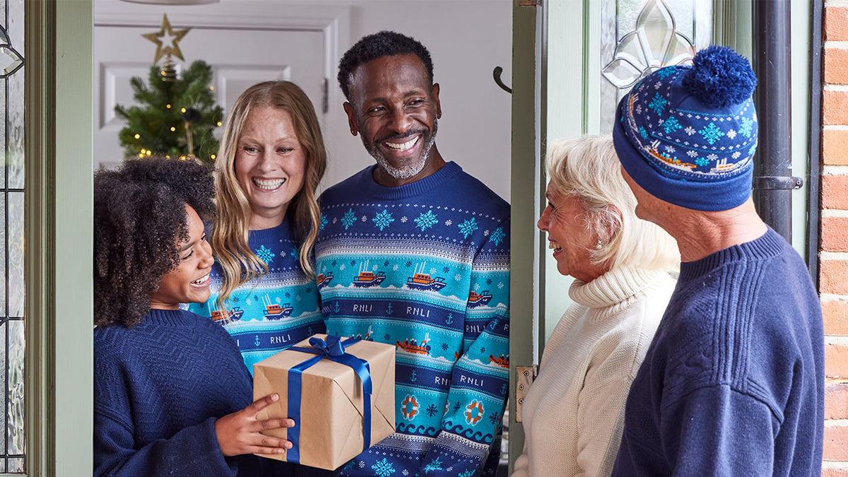  Family in matching blue RNLI Christmas sweaters with a Christmas tree and gift exchange. 