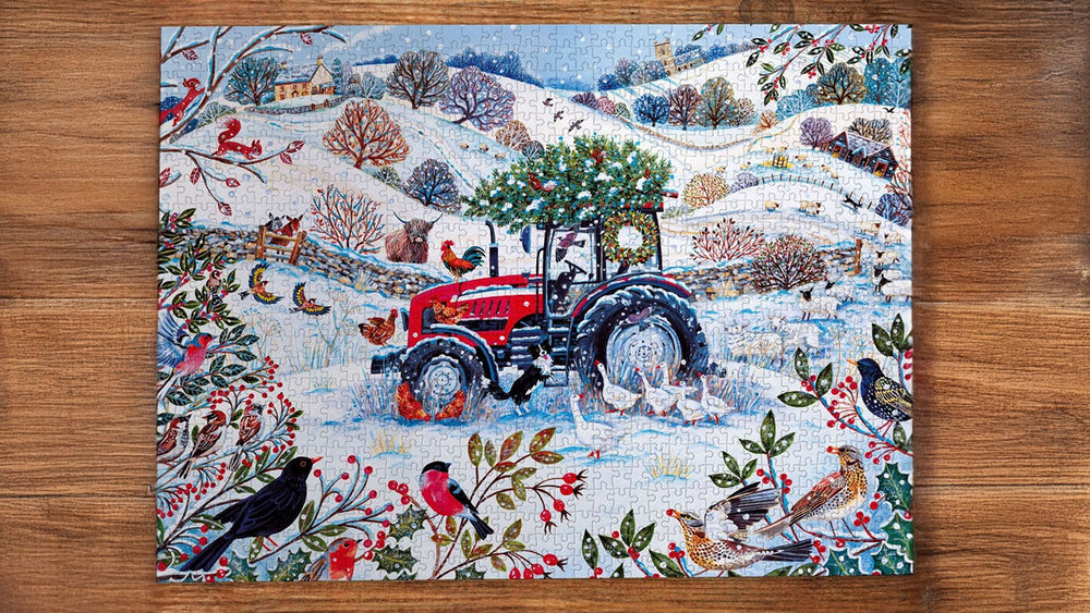  A completed jigsaw puzzle featuring a winter farm scene with a red tractor, snowy hills, birds, and festive foliage, displayed flat on a brown wooden surface. 
