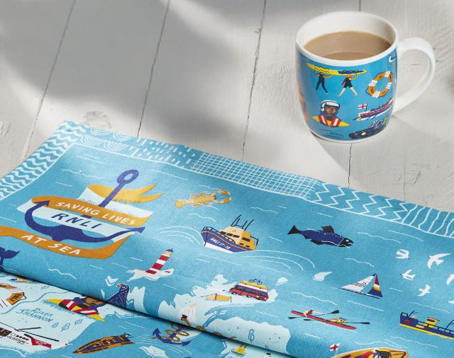  Blue Icons Map Tea Towel with maritime designs and a matching mug on a light wooden surface. 