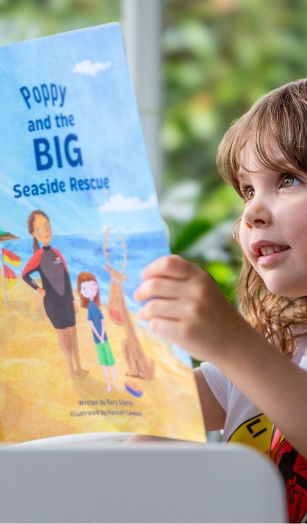  A young girl reading a personalised book called 'Poppy and the Big Seaside Rescue' 