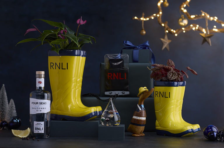 A selection of RNLI gifts in front of a navy background with festive lights, with wrapped presents tied in navy bows.