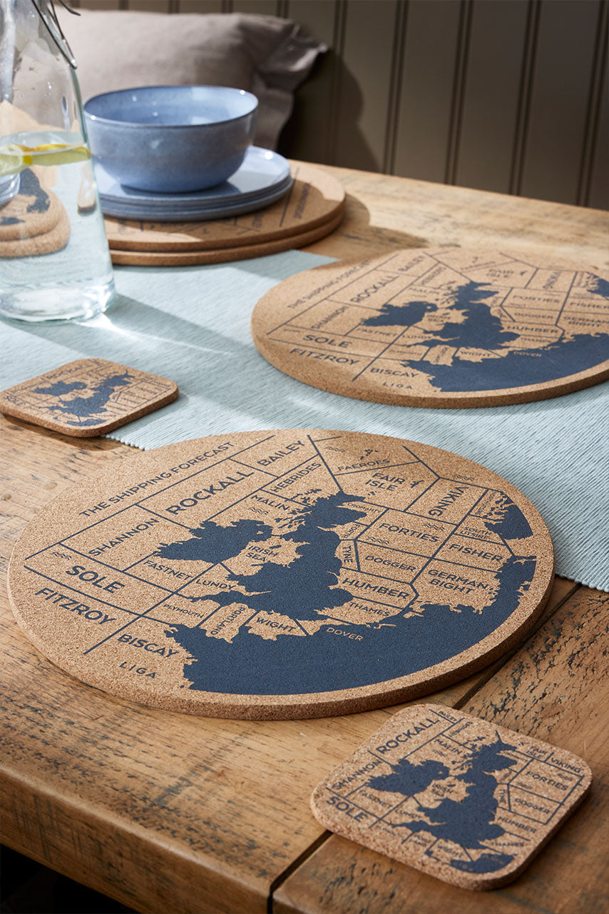  cork placemats and coasters with shipping forecast designs lay out on a wooden table. 
