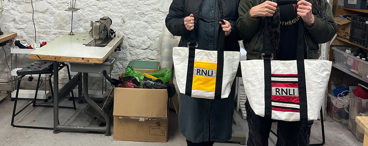 Two people, the makers of the bags holding freshly created RNLI repurposed tote bags in a workshop setting.