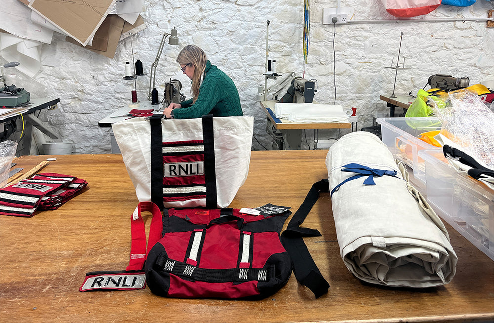  RNLI gear including a life jacket and bag on a table with a person working on sewing the jackets together to make the bag in the background. 