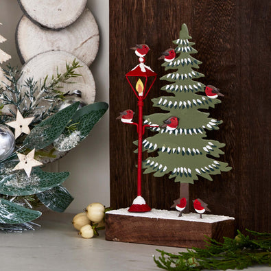Decorative Christmas scene with a tree, lamp, and birds on a wooden background