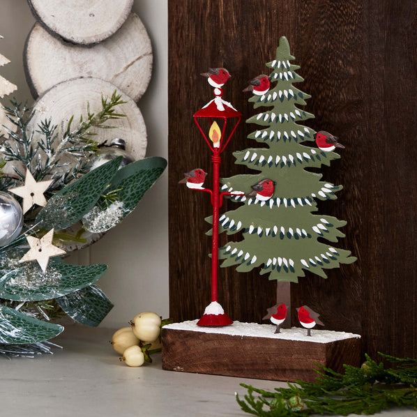 Decorative Christmas scene with a tree, lamp, and birds on a wooden background