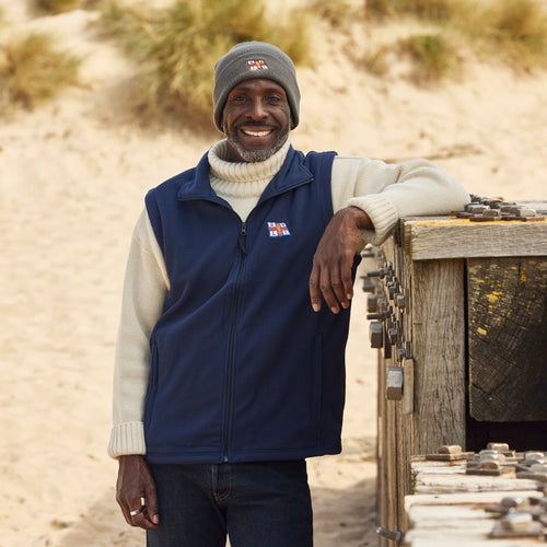 A man at the beach wearing a navy fleece gilet with the RNLI flag on the left chest. 
