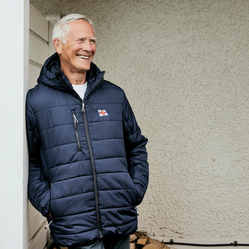 A man leaning against a wall outside wearing a navy RNLI Jacket with a full zip and a hood. 