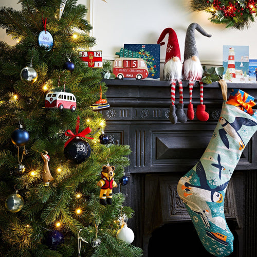 A large Christmas tree in front of a fireplace with RNLI decorations hung on the branches.