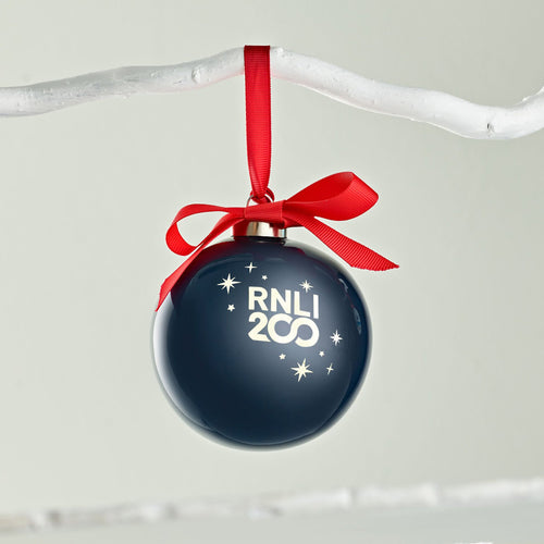 A navy bauble with RNLI 200 printed on it in silver,  tied to a branch with a red ribbon