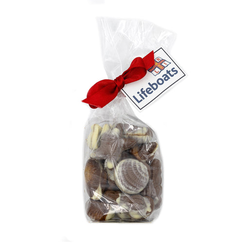 A clear bag tied with a ribbon and filled with chocolates in the shape of seashells.