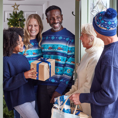 A family gathering in a doorway with people wearing festive sweaters and holding gifts
