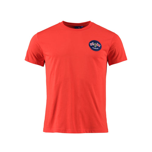 A red short sleeved t-shirt with a navy embroidered badge on the left chest featuring the RNLI flag. 