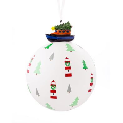 An RNLI glass bauble with a 3D ceramic lifeboat on the top. The bauble is white with red lighthouses and green Christmas trees on it. 