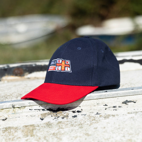 A baseball cap laid on top of a rusty white boat. The navy cap has the RNLI Membership logo embroidered on the front.