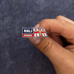 A close up of someone's hand holding a metal RNLI Membership Pin Badge in red, white and navy.