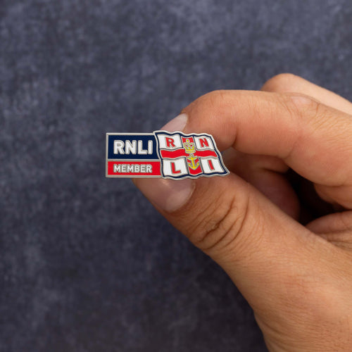 A close up of someone's hand holding a metal RNLI Membership Pin Badge in red, white and navy.
