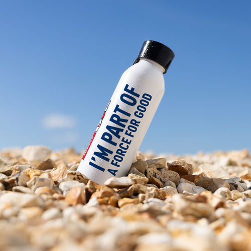 A white RNLI Membership Water Bottle sat on a stoney beach.