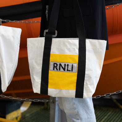 Model holding a white tote bag with black stripes and a red, reflective 'RNLI' logo. Made out of repurposed lifejackets