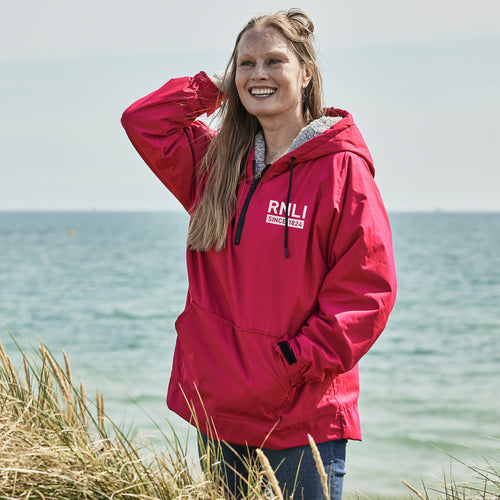 A woman standing by the beach wearing a pink RNLI Waterproof Fleece Hoodie.
