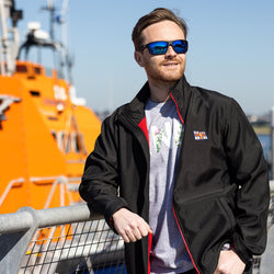 Model wearing Dirty Dog Axle Polarised Sunglasses, Black/Blue and RNLI Men's Ablaze Softshell Jacket, Black/Red