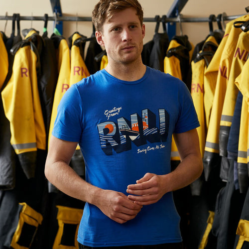 A man standing in front of RNLI lifeboat kit wearing a royal blue tshirt with an RNLI print on the chest.
