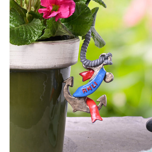 A resin anchor shape in red, blue and gold. It has a banner running around the anchor that says, 'RNLI'. The pot hanger is hooked over the edge of the pot by a resin, rope shaped, hook