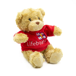 A light brown teddy bear wearing a bright red t-shirt with the RNLI Lifeboats logo on the front.