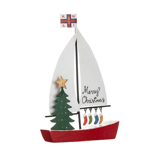 A red sailing boat with white sails with a green Christmas tree on the deck