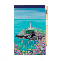 An A5 notepad with a painting of a lighthouse on top of a cliff on the cover. There are pink and yellow wildflowers in the foreground.