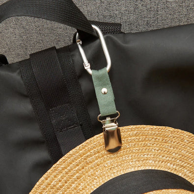 A straw hat clipped to a backpack with the travel hat clip.
