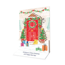 A pop-up Christmas card with an illustration of a red front door decorated with a wreath, Christmas trees and presents.
